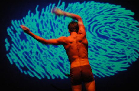 mixed body dancer stands posed in front of digital finger print projected on screen