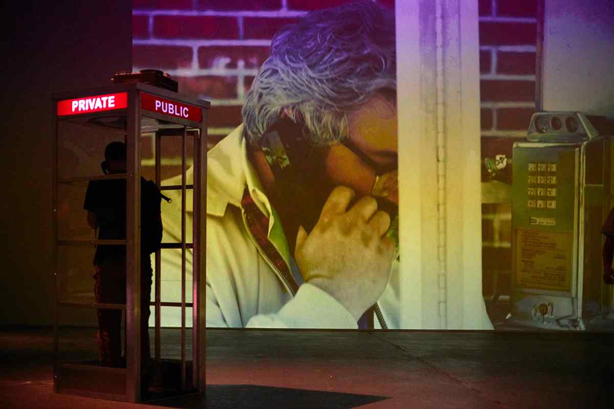 A projection of a man talking on the phone in front of a phone booth.