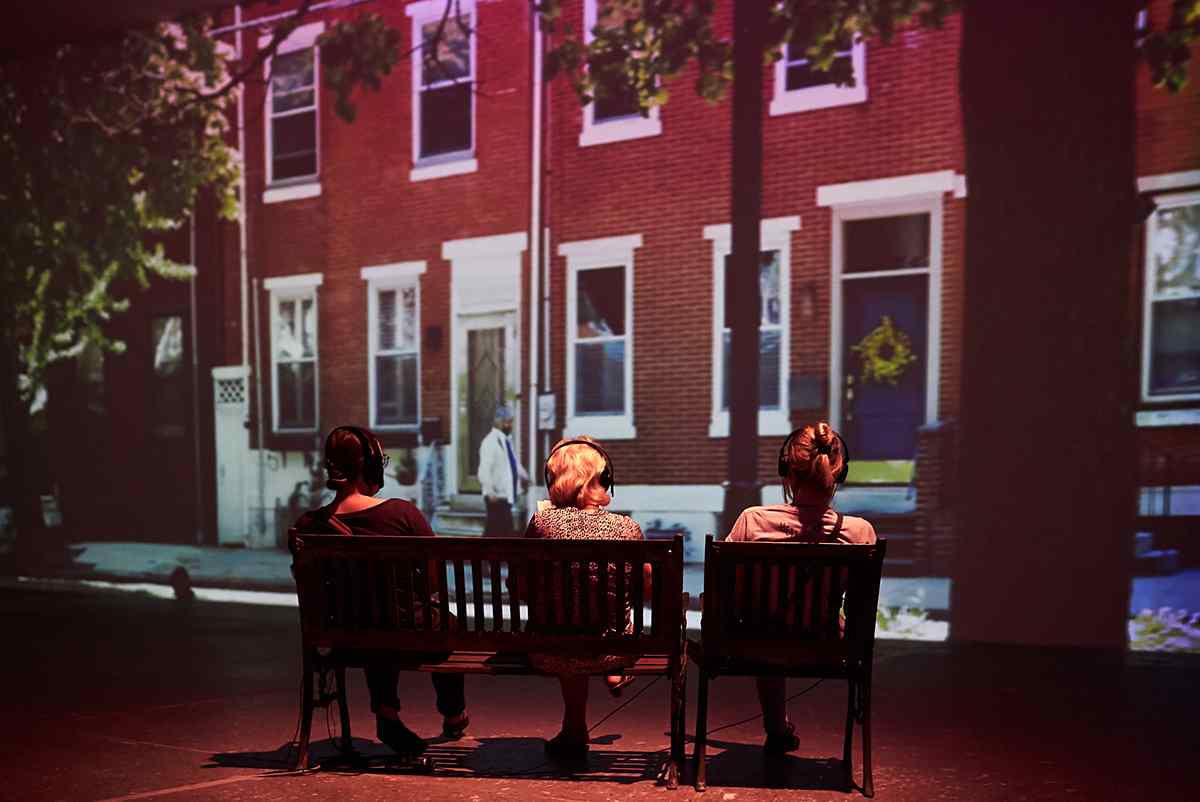 Three women sitting on a bench in front of a projection.