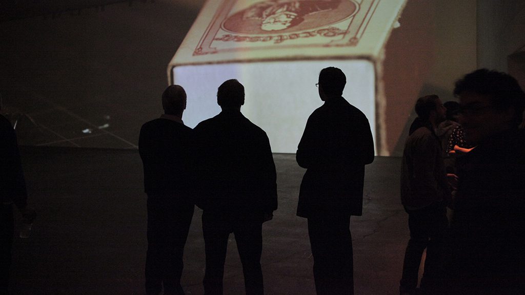 Silhouette of gallery visitors against large projection of matchbox