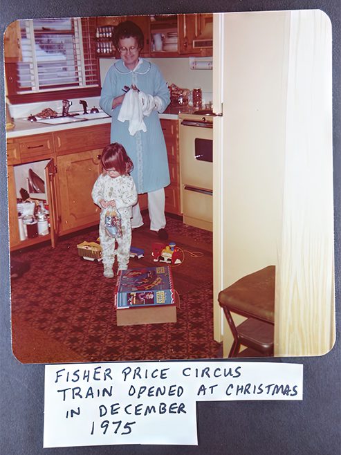 photo of young girl and older woman in kitchen with toy train on the floor. under the photo it says Fisher Price Circus Train Opened at Christmas in December 1975."